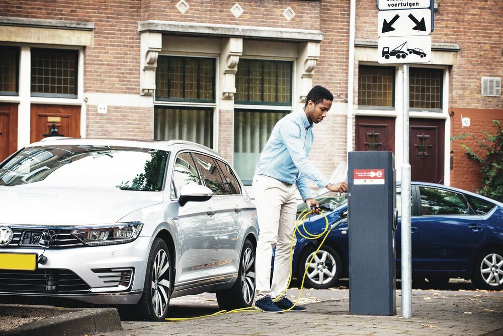 A young man wearing a casual business outfit, plugging in an EV in the streets of Amsterdam.