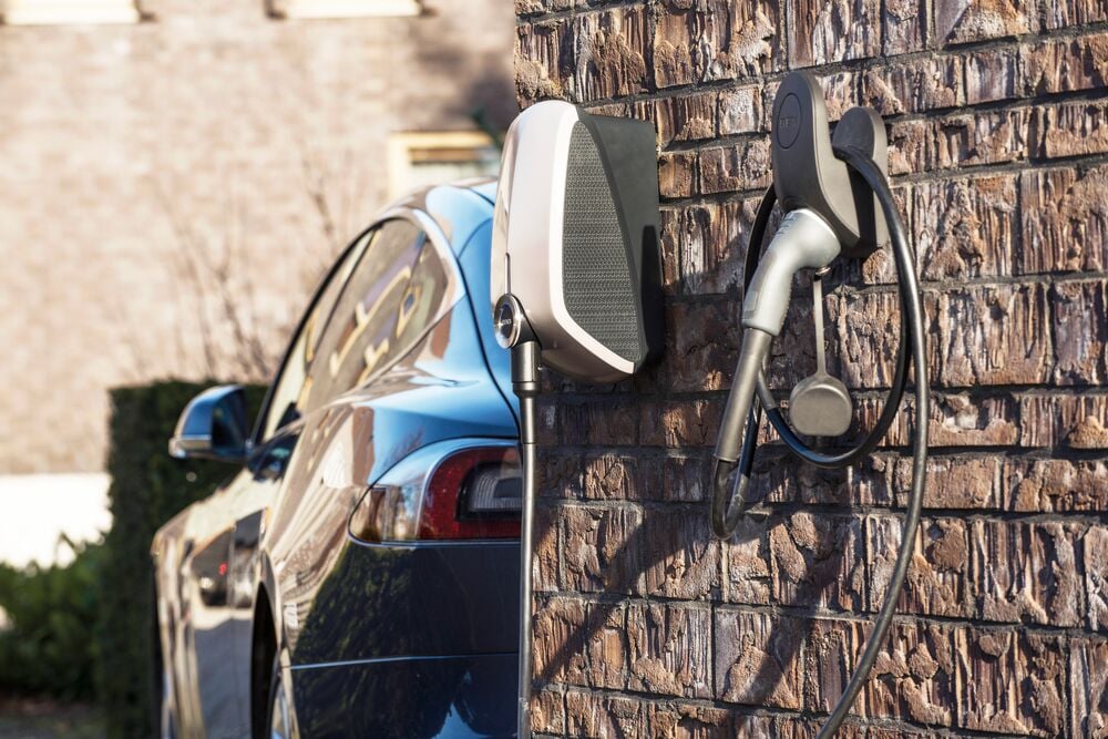 De EVBox Elvi-laadpaal aan de muur van een huis met een elektrische auto, van het merk Tesla, op de oprit.