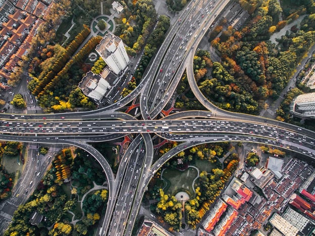 Birds eye view looking down onto a busy motorway junction with roads crossing over each other. There are autumnal trees surrounding the junction.