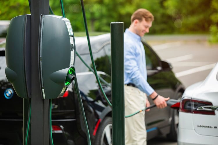 EVBox BusinessLine Ladestation mit einem Mann im Hintergrund, der sein weißes Elektroauto auflädt.