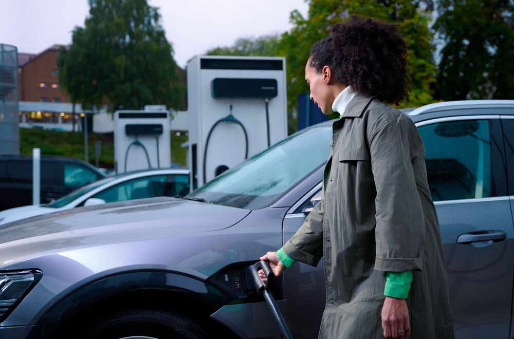 A woman plugs in the cable of an EVBox Troniq Modular charging station into her EV.