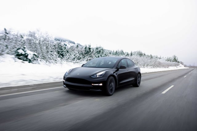 A Tesla Model 3 cruising along the road in a snowy day.