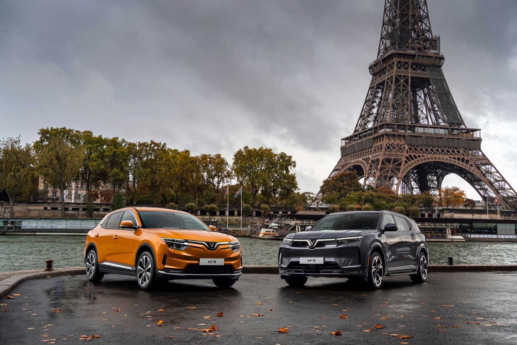 An orange and black Vinfast VF9 parked in front of the Eiffel Tower in Paris. 