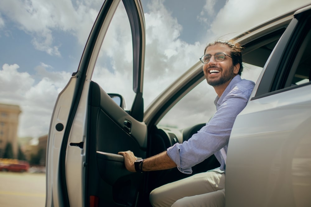 A smiling man sitting in his EV opens the driver door