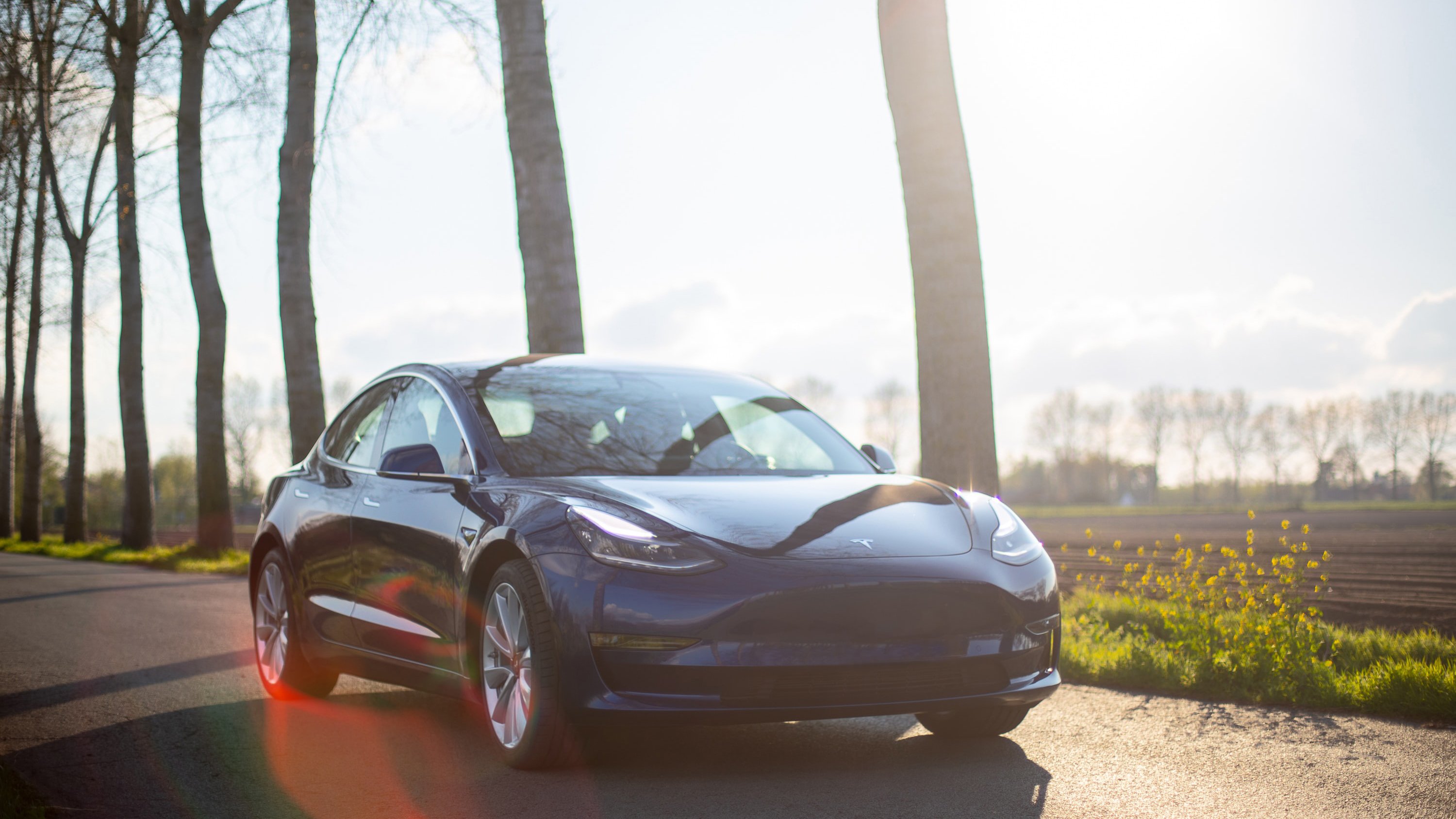 A Tesla Model 3 driving on a country road.
