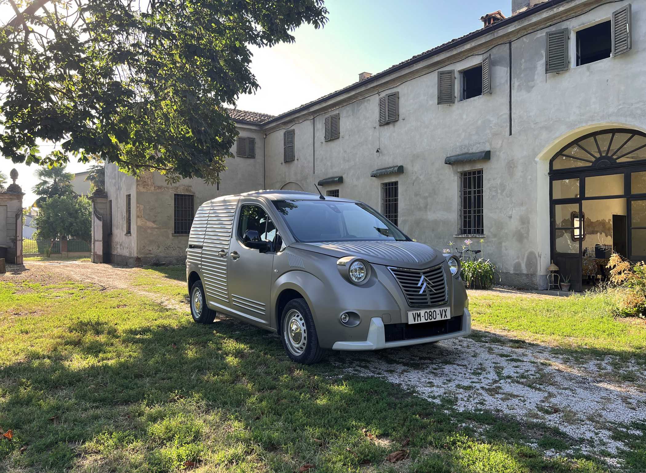 A Fourgonnette Panel Van parked beside an old house under the shade of a tree.