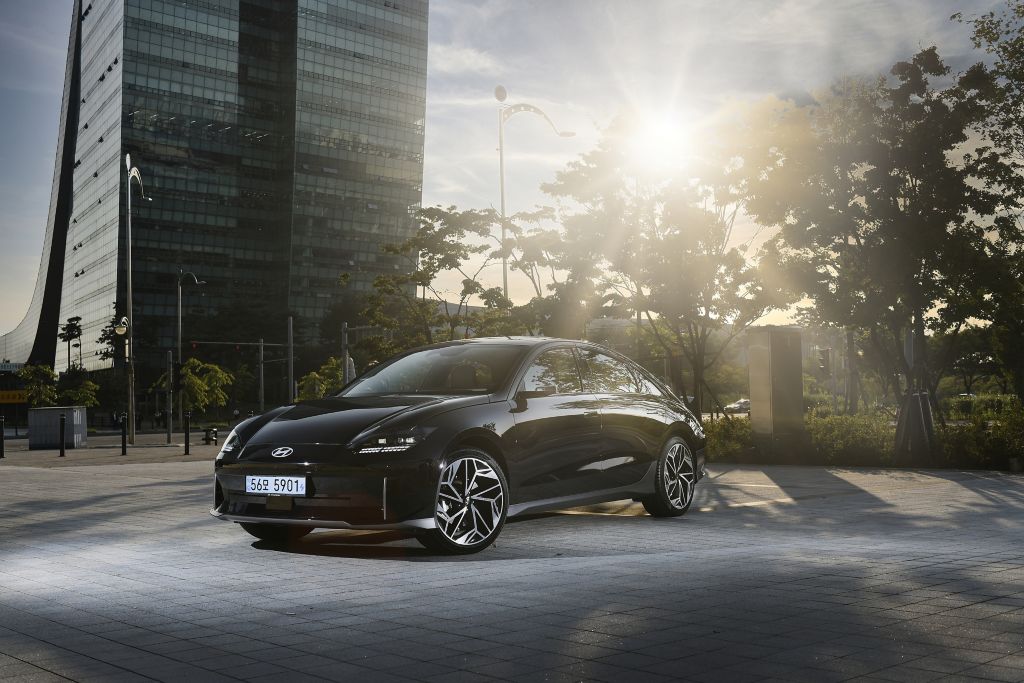 A black Hyundai IONIQ 6 parked in front of a business area with the late afternoon sun shining through the trees in the background.