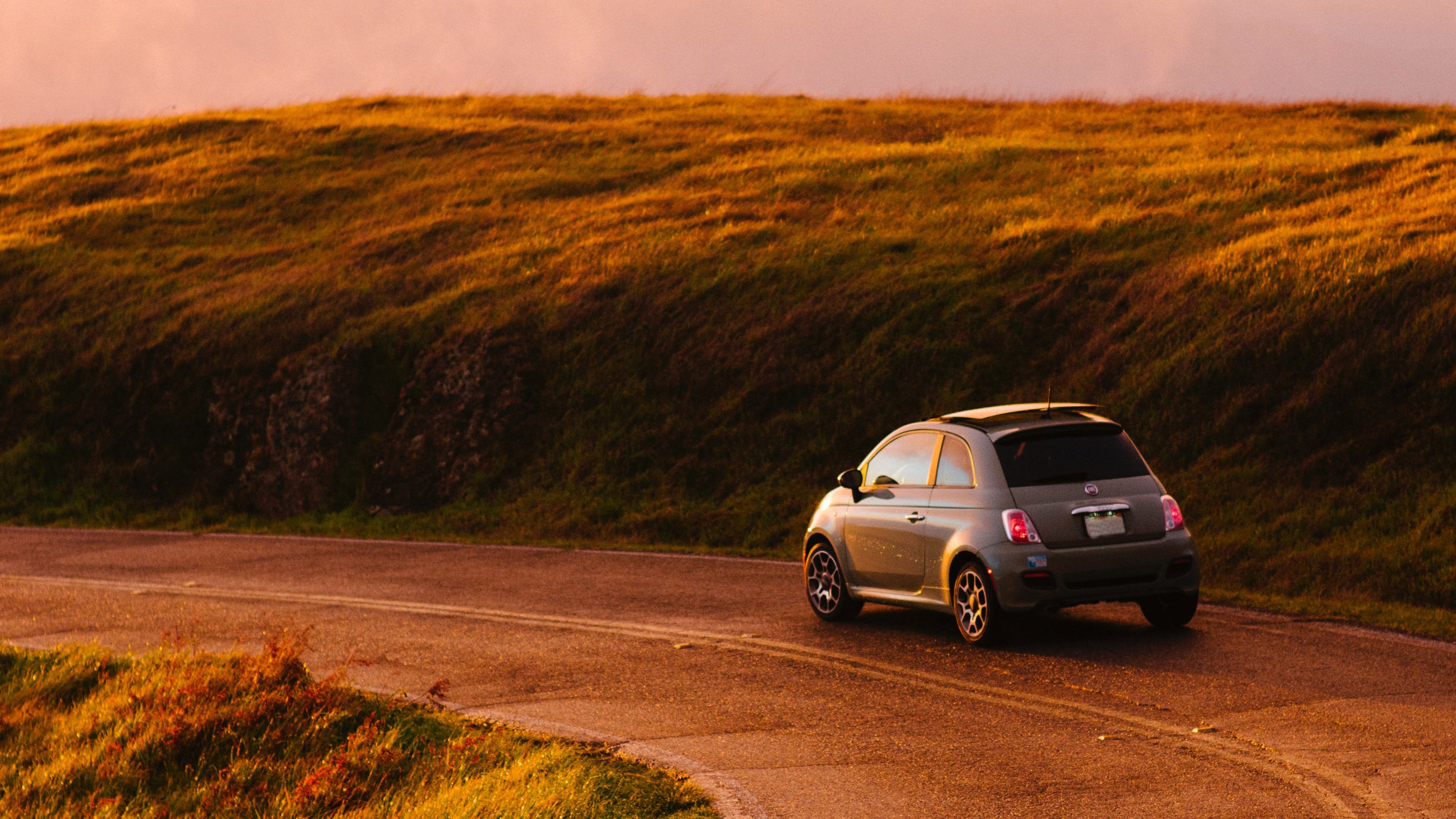 A Fiat taking a turn on a road during sunset.