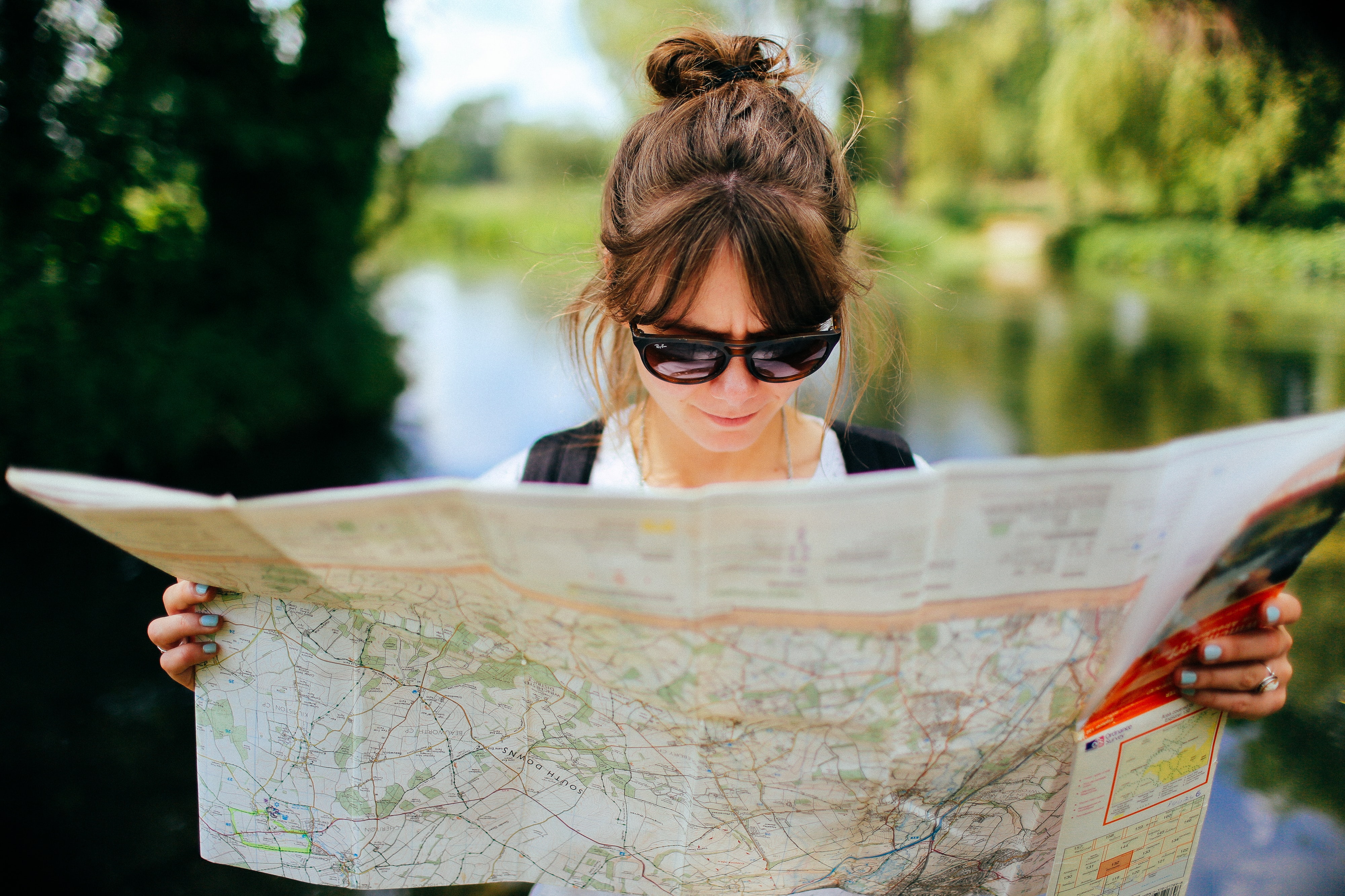 Eine Frau mit Sonnenbrille steht vor einem See und zeichnet ihre Route auf einer Karte ein.
