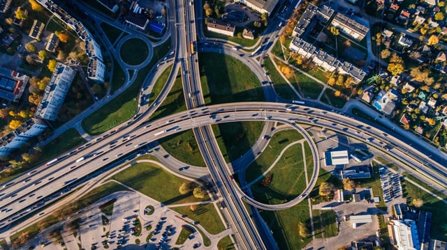 an aerial shot of cars driving on a busy intersection in a city surrounded by patches of green.