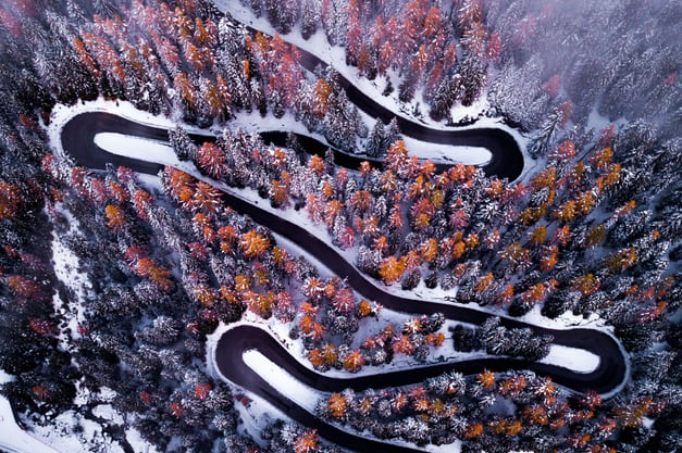 An arial shot of a snow-lined highway in the forest in winter. 