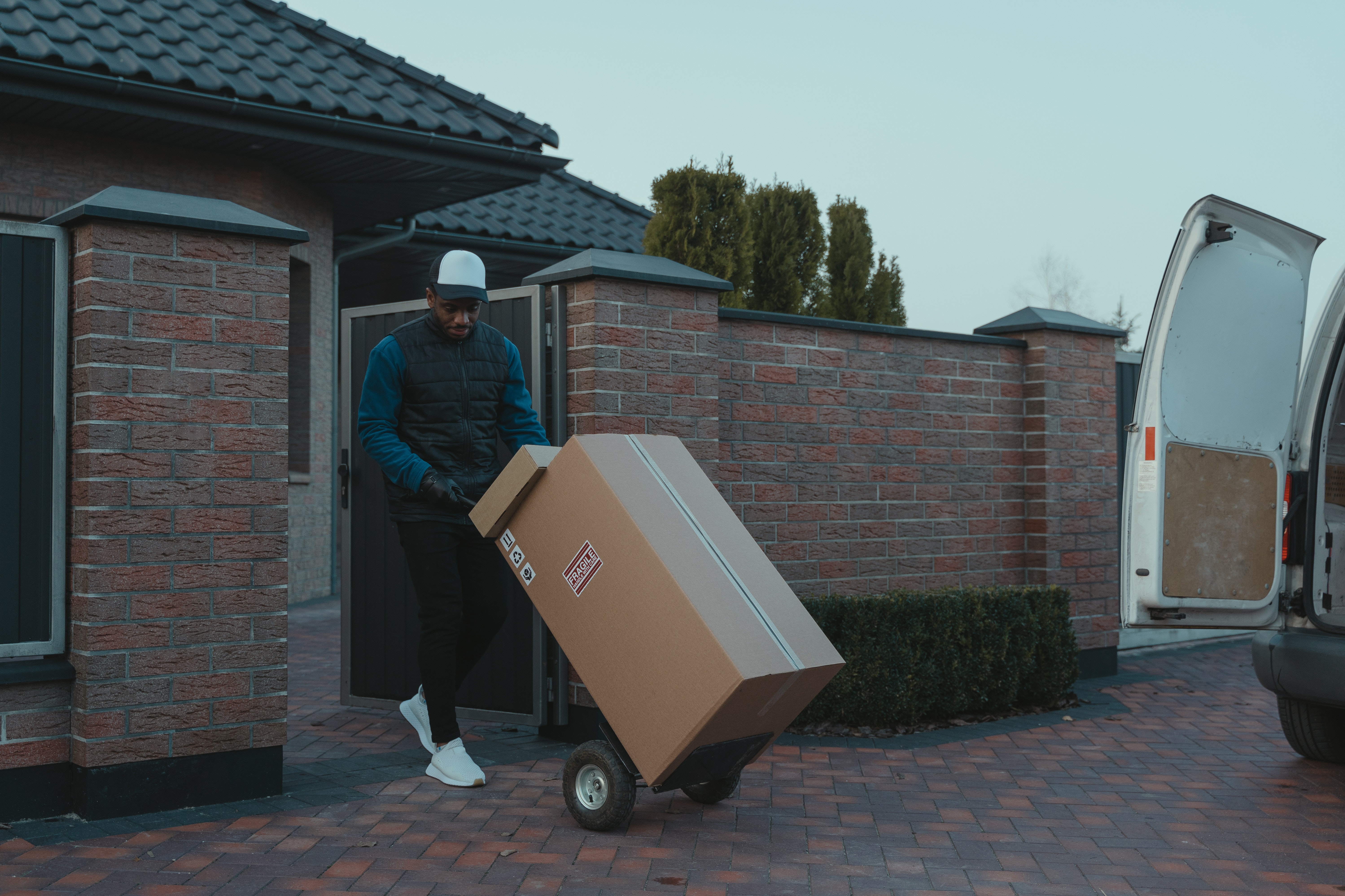 Un repartidor que descarga un paquete de un vehículo comercial ligero para realizar una entrega en una dirección residencial.