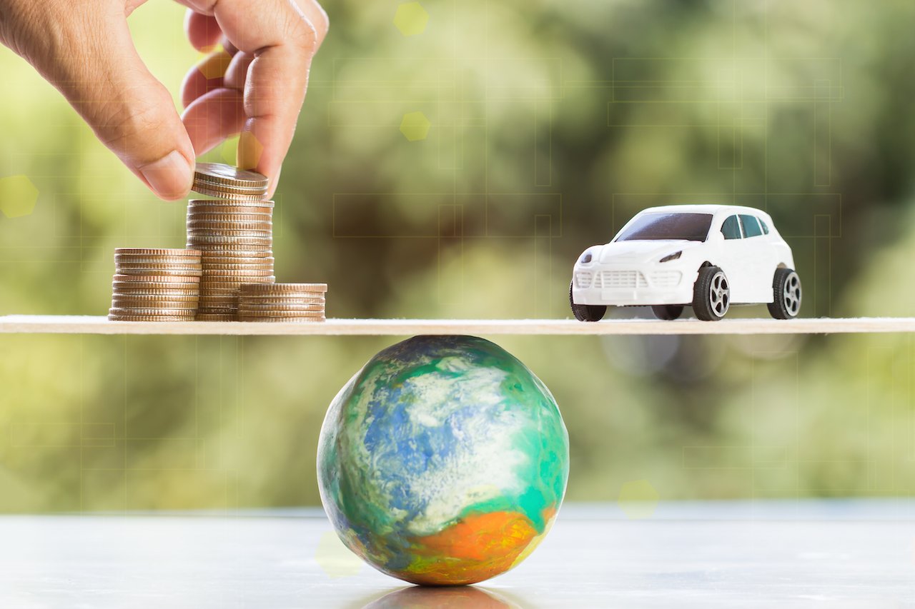 A toy car and a stack of coins balancing on a scale placed on top of a miniature planet earth.