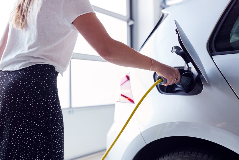Een vrouw steekt een laadkabel in haar elektrische auto die in een garage staat.