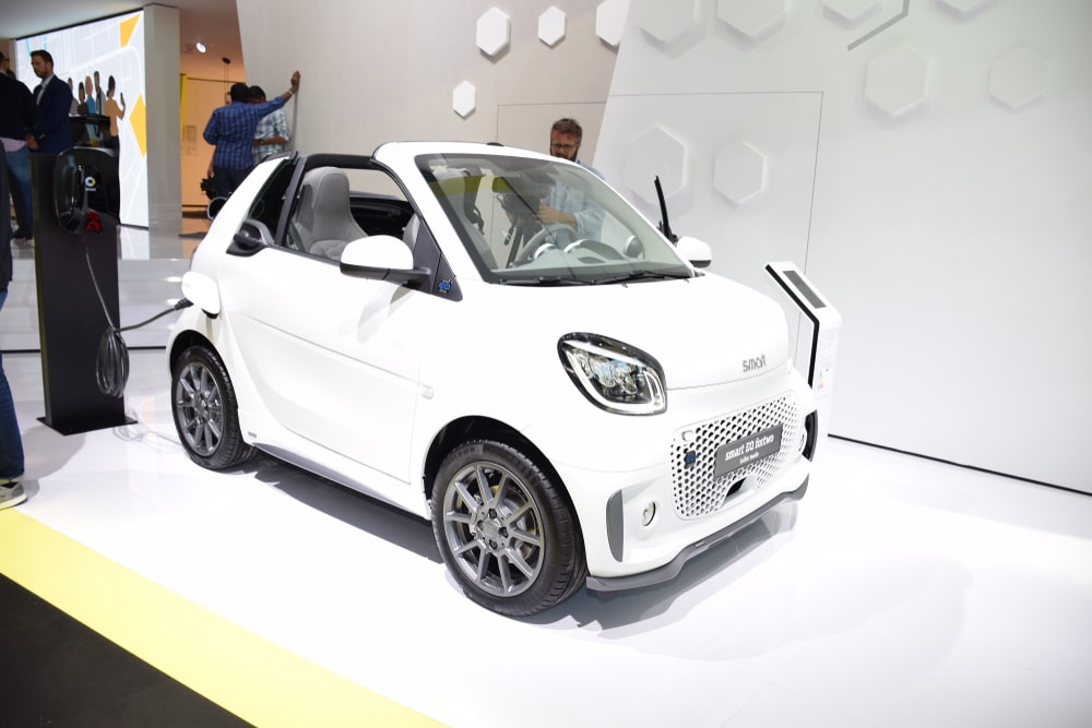 A white Smart EQ fortwo cabrio parked at a tradeshow.