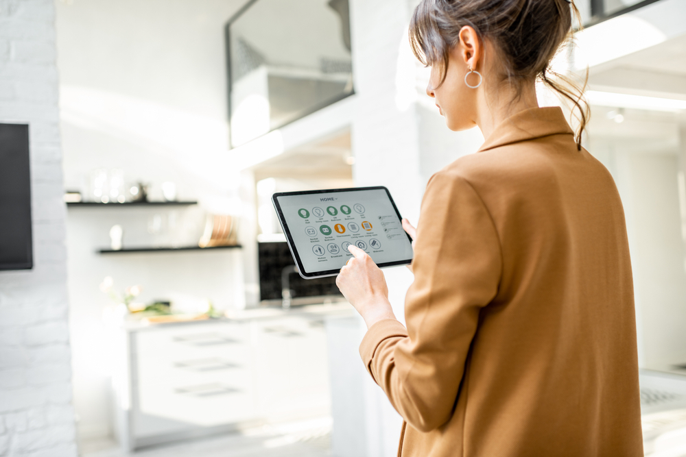 A woman is holding a tablet and selecting smart features for the house.