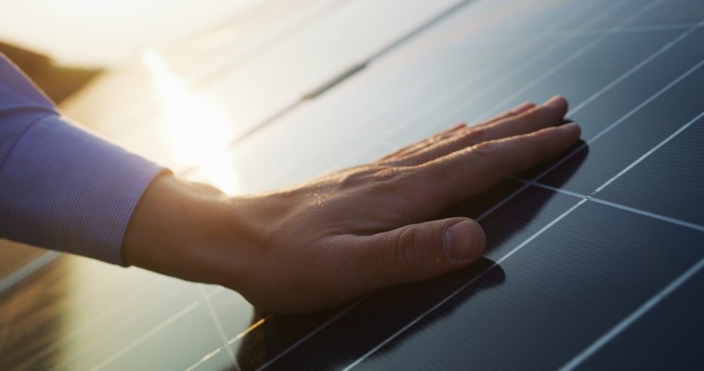 Eine Nahaufnahme einer Hand, die bei Sonnenuntergang ein Solarpanel berührt.