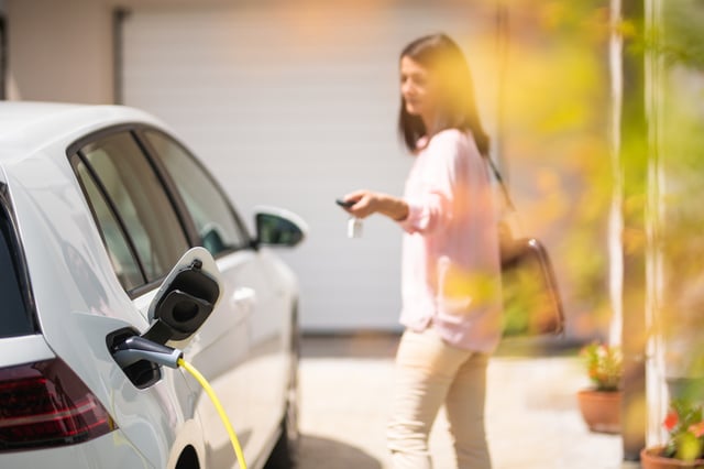 A woman is locking her car which is charging outside a house.