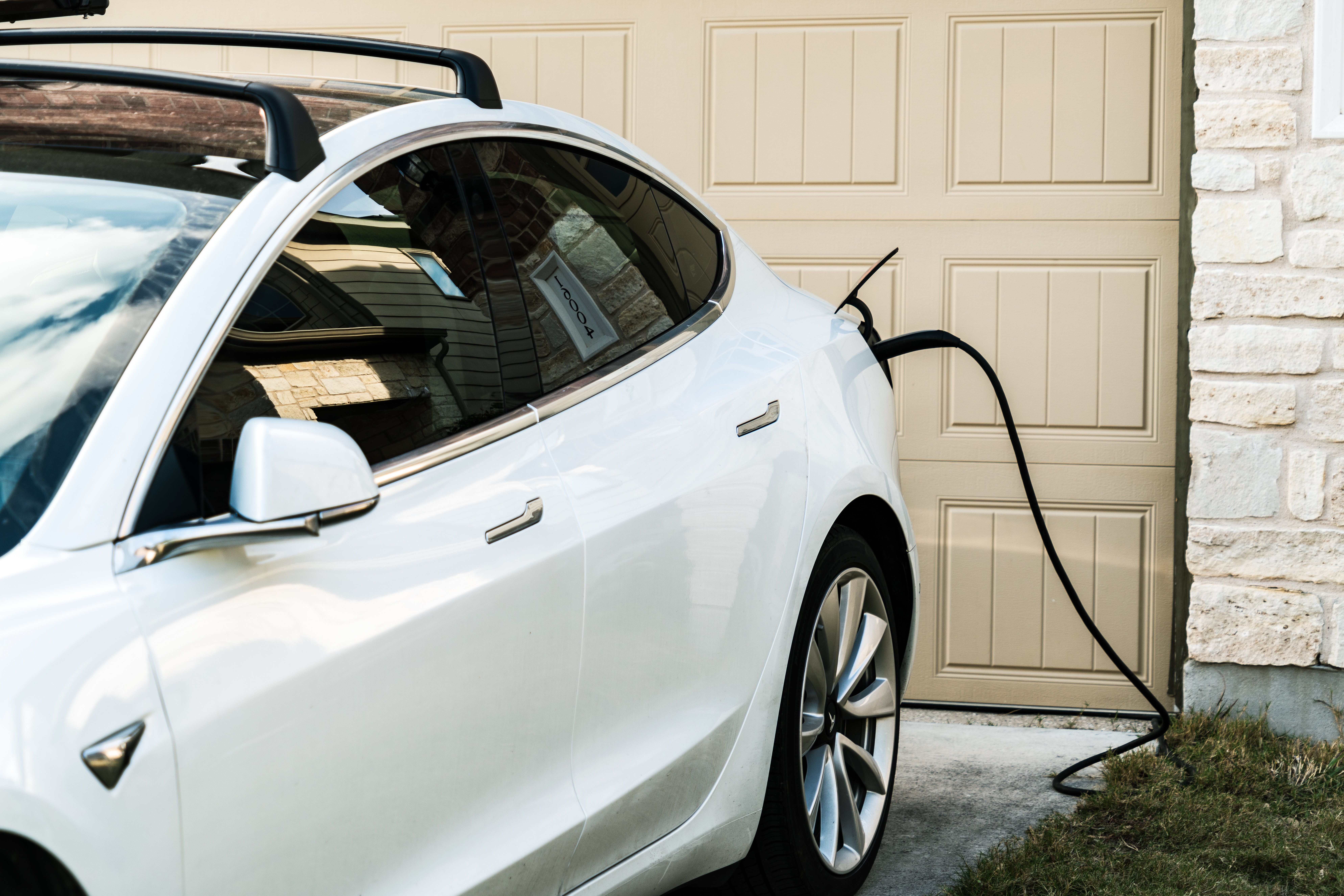 A closeup of a white car charging at home outside a garage.