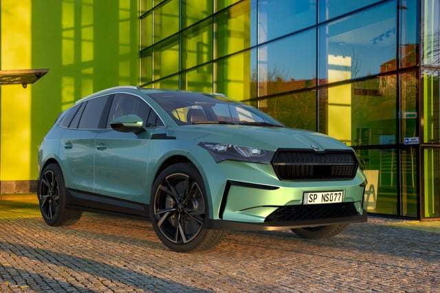 The Skoda Enyaq iV electric SUV parked on brick road next to a large windowed building and green wall.