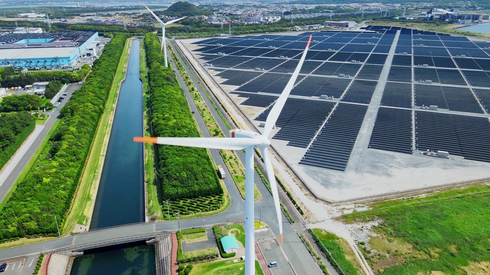 An aerial shot of an industrial complex with two wind turbines and solar panels.