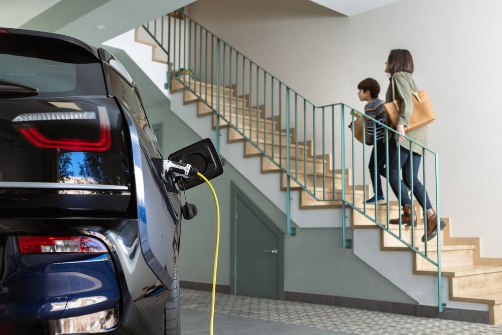 A woman and her son are climbing the stairs from the garage where an electric car is charging.