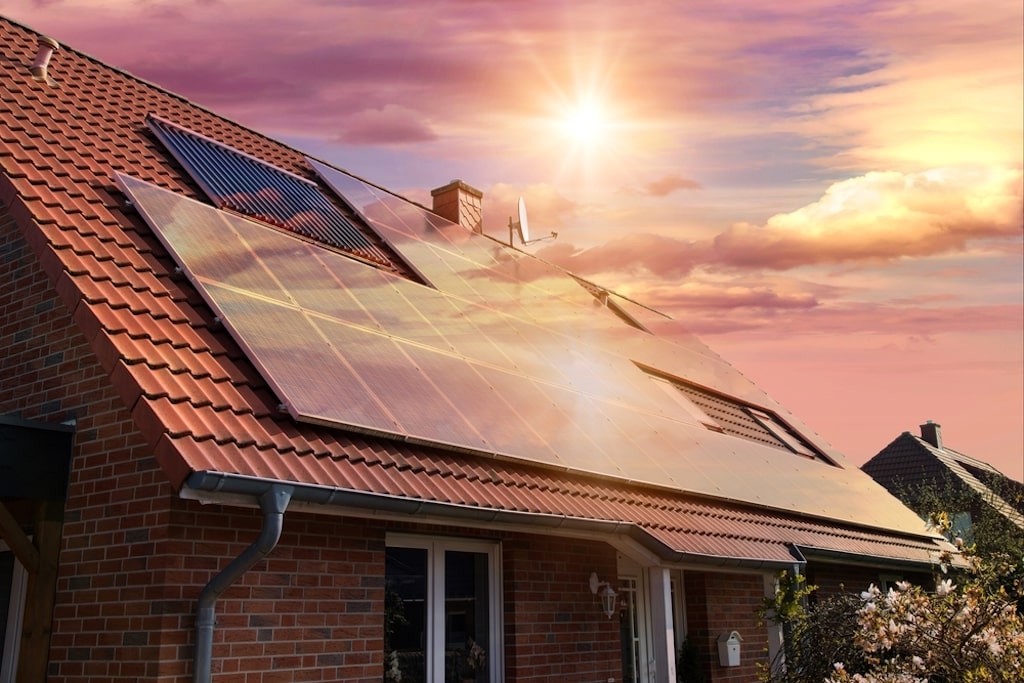 solar panels, photovoltaics on a red roof of a house with a a beautiful sky and the setting sun in the background..