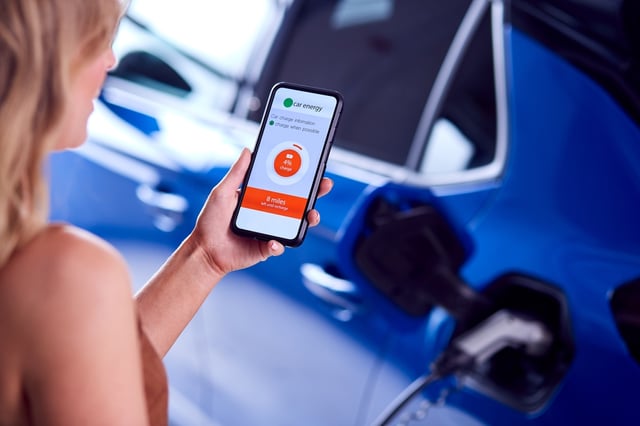 A close-up of a woman holding her smartphone and checking the charging status of her electric car through an EV charging app.