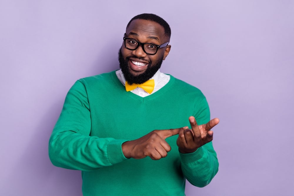 A smiling man wearing a casual sweater and a bowtie explaining something