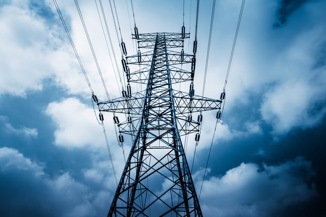 A professional photo of an high-voltage tower with clouds in the background.