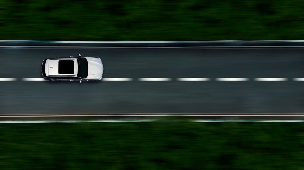 Panning shot of car driving on the road taken from above.