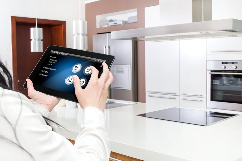 Een persoon in de keuken beheert de slimme huishoudelijke apparaten met een tablet.