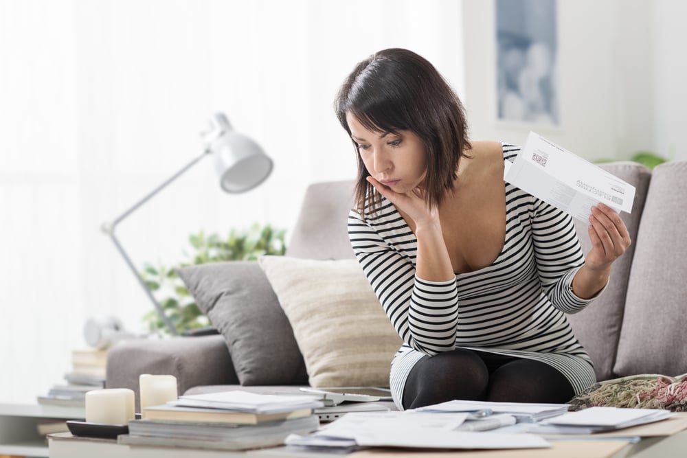 Eine Frau prüft einige Energierechnungen, während sie auf einem Sofa in ihrem hellen Wohnzimmer sitzt.