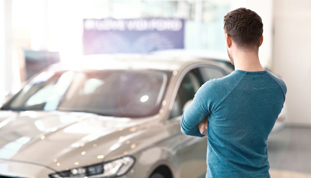Young man looking at a new car in a showroom.