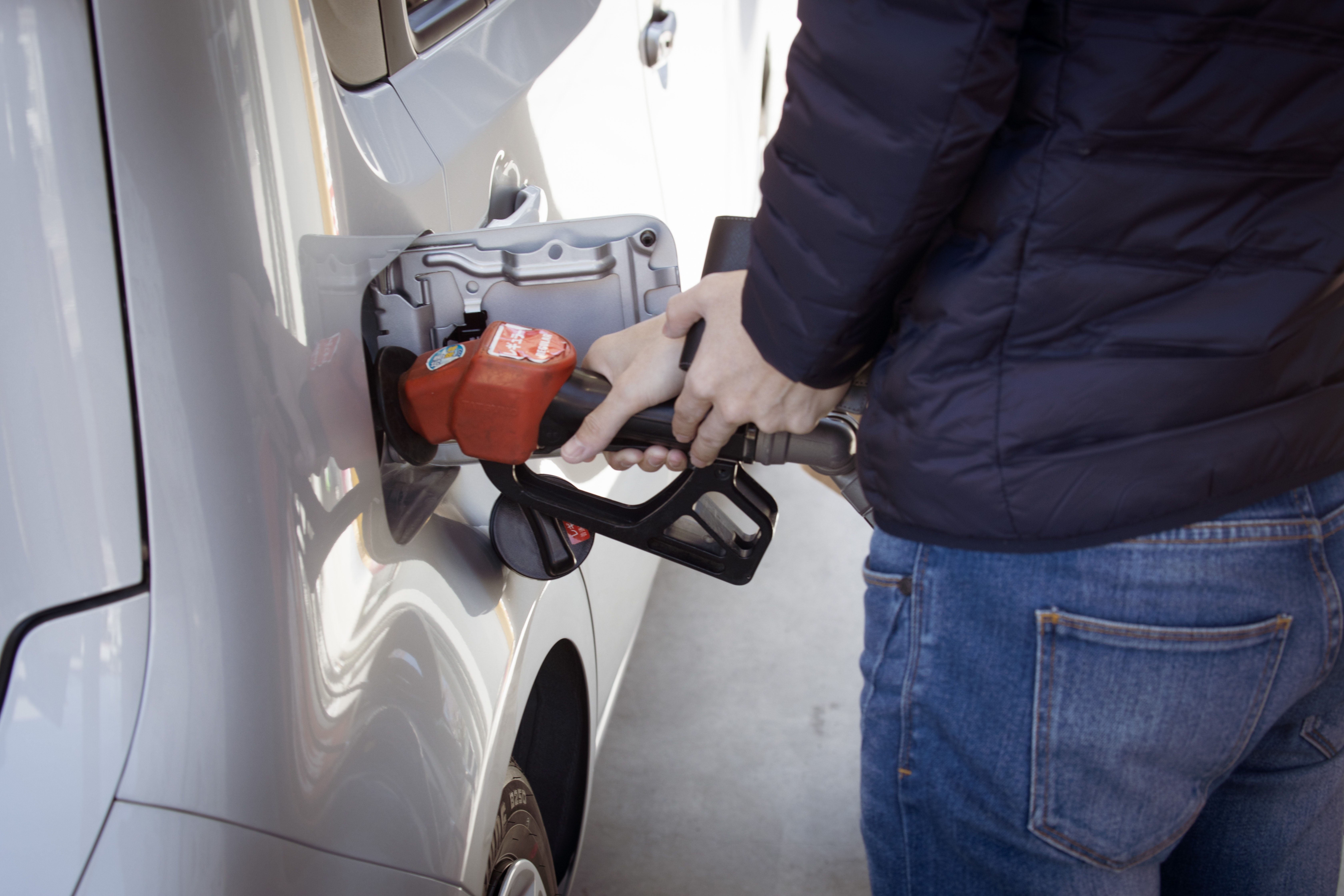 A person filling their internal combustion engine vehicle with carbon-emitting fossil fuels.